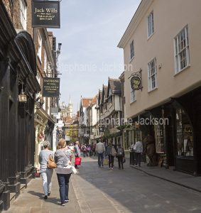 Narrow street and shops with pedestrians / shoppers in the heart of the historic city of York in Yorkshire, England.