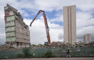 Crane demolishing old apartment tower block with new building rising from the rubble in the city of Glasgow in Scotland.