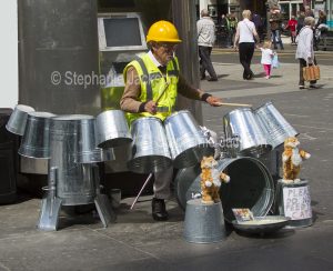 Unusual musical instruments, A busker, known as the Techno Tin Bin Man, playing music on an array of upturned buckets in the city of Glasgow in Scotland.
